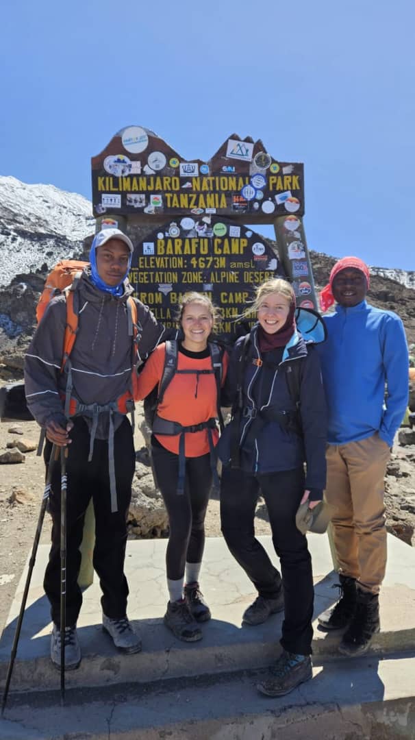 Four hikers with backpacks standing beside a wooden sign on rocky ground