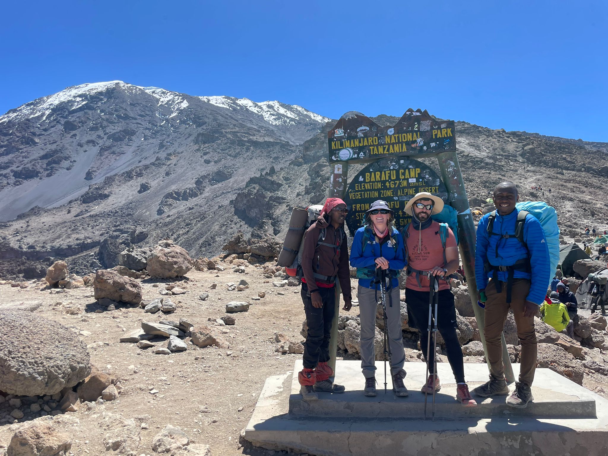 Four hikers standing in a rocky landscape with a snowy mountain behind