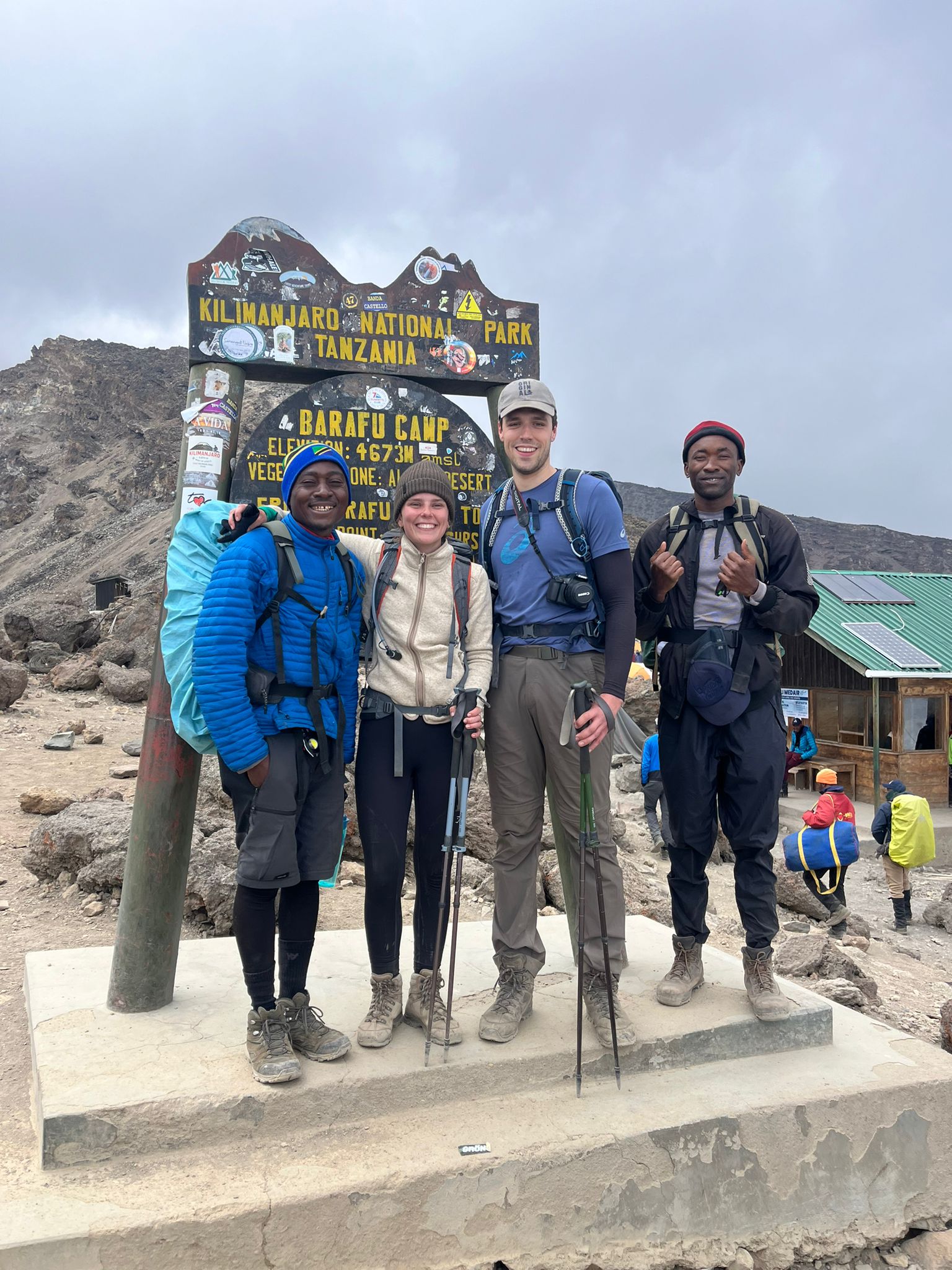 Four climbers posing beside a wooden sign on rocky high ground