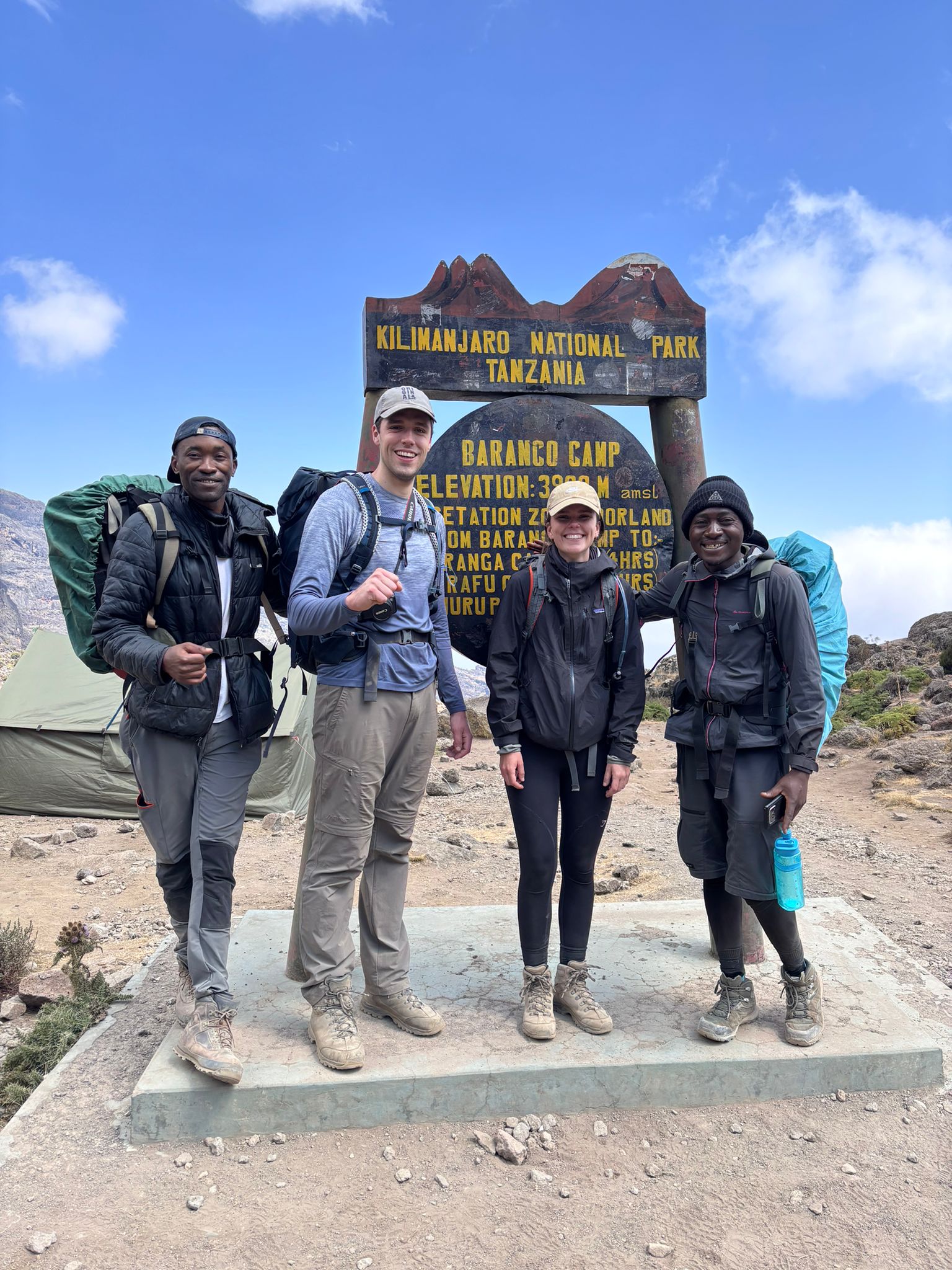 Four hikers standing together beside a wooden mountain sign