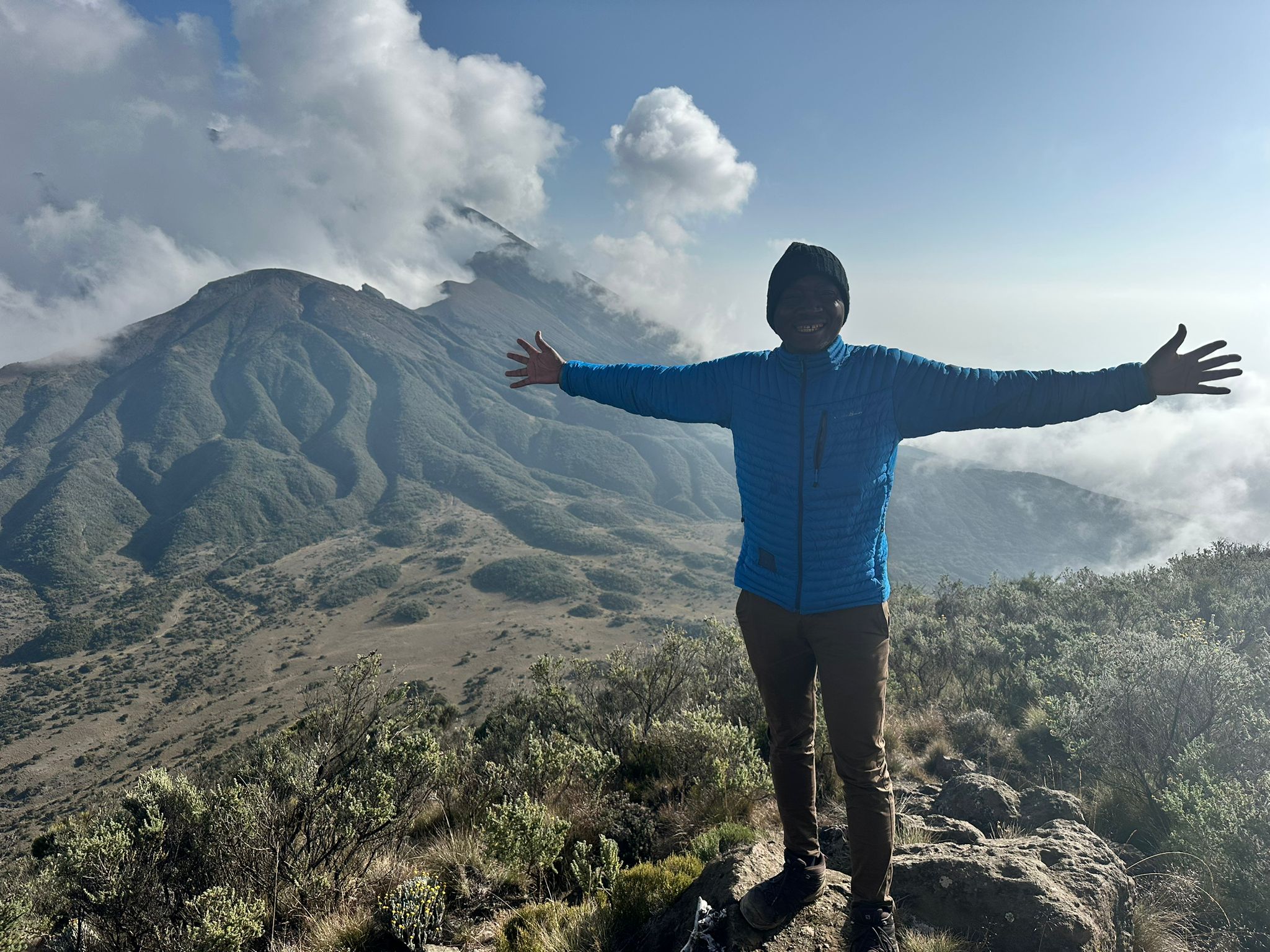 A guide standing with arms open before a rugged mountain landscape