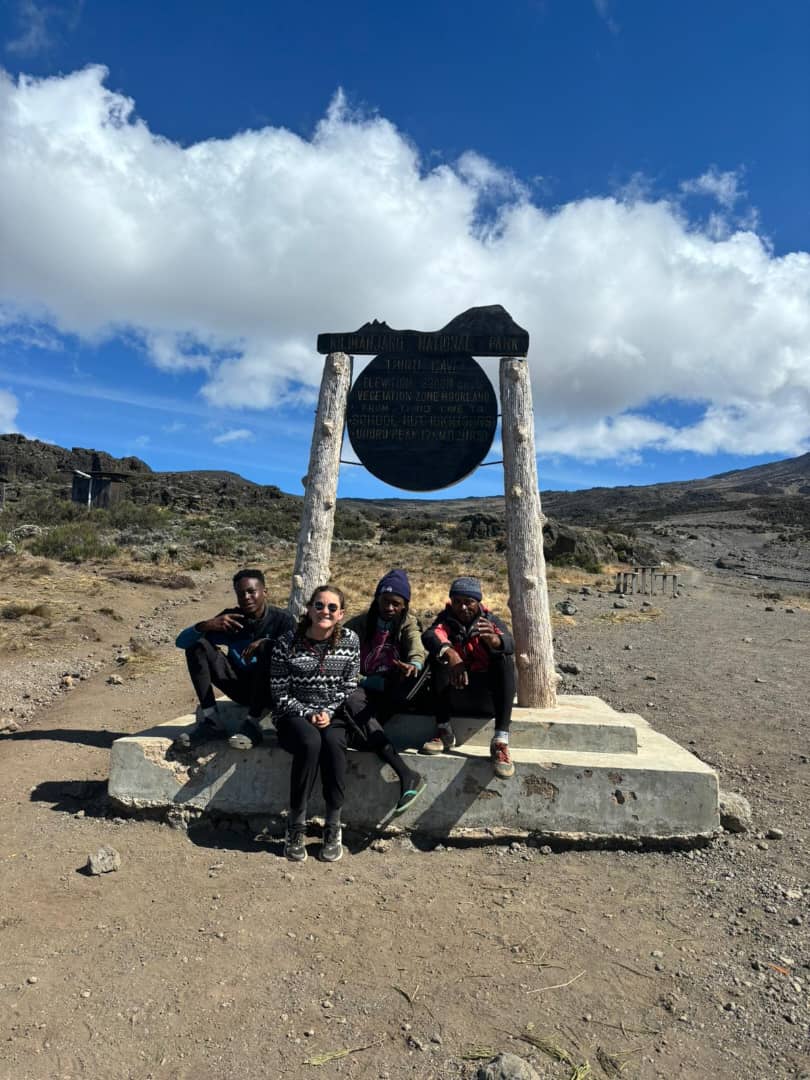 A group resting beneath a hanging metal bell in a rocky landscape