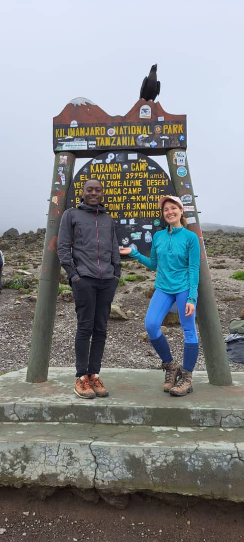 Two climbers standing with trekking poles beside a wooden mountain sign