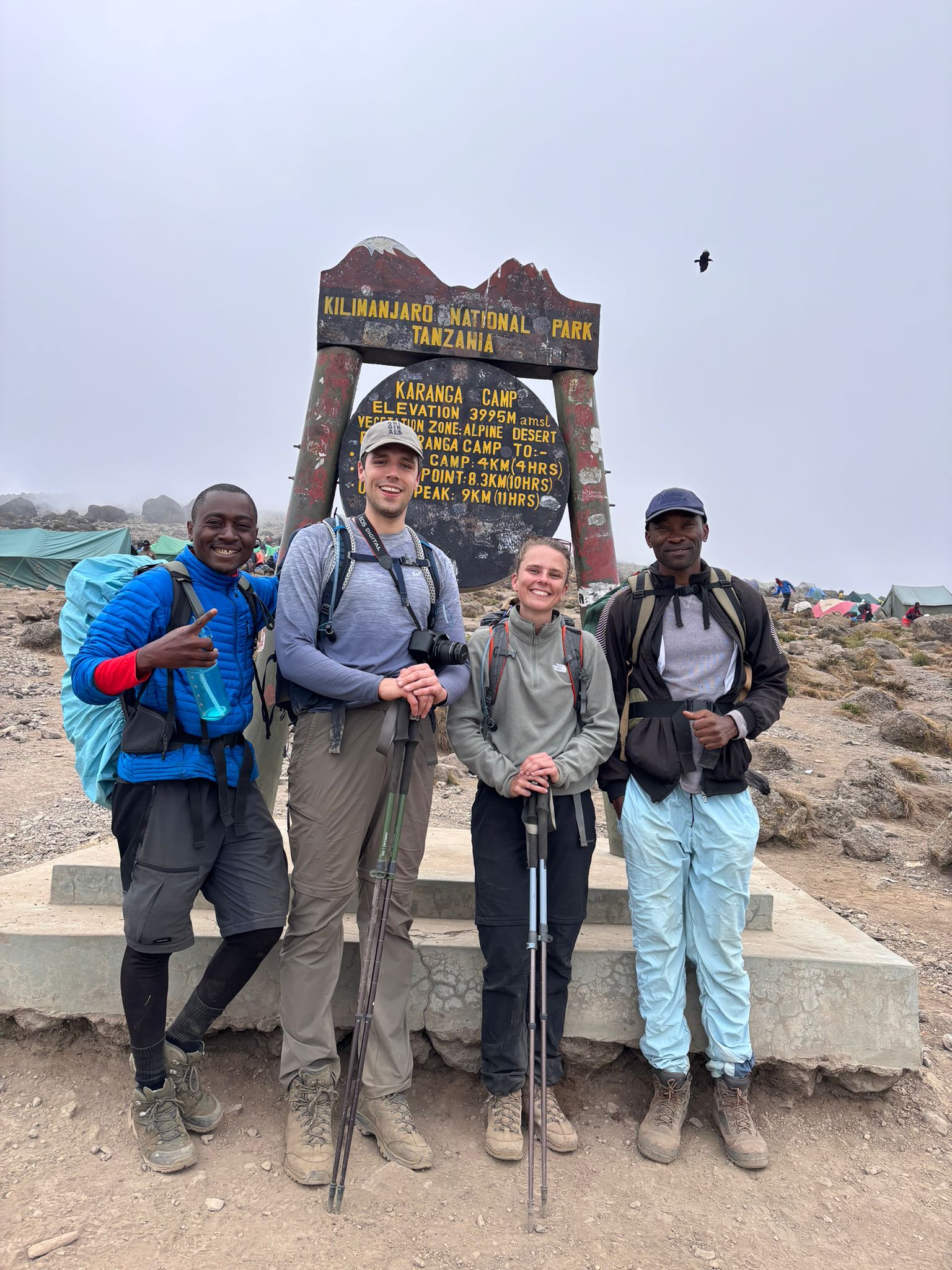 Four climbers posing beside a wooden trail sign