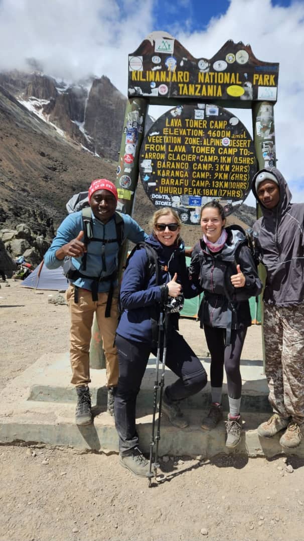A group of climbers posing beside a sign in a rocky mountain landscape