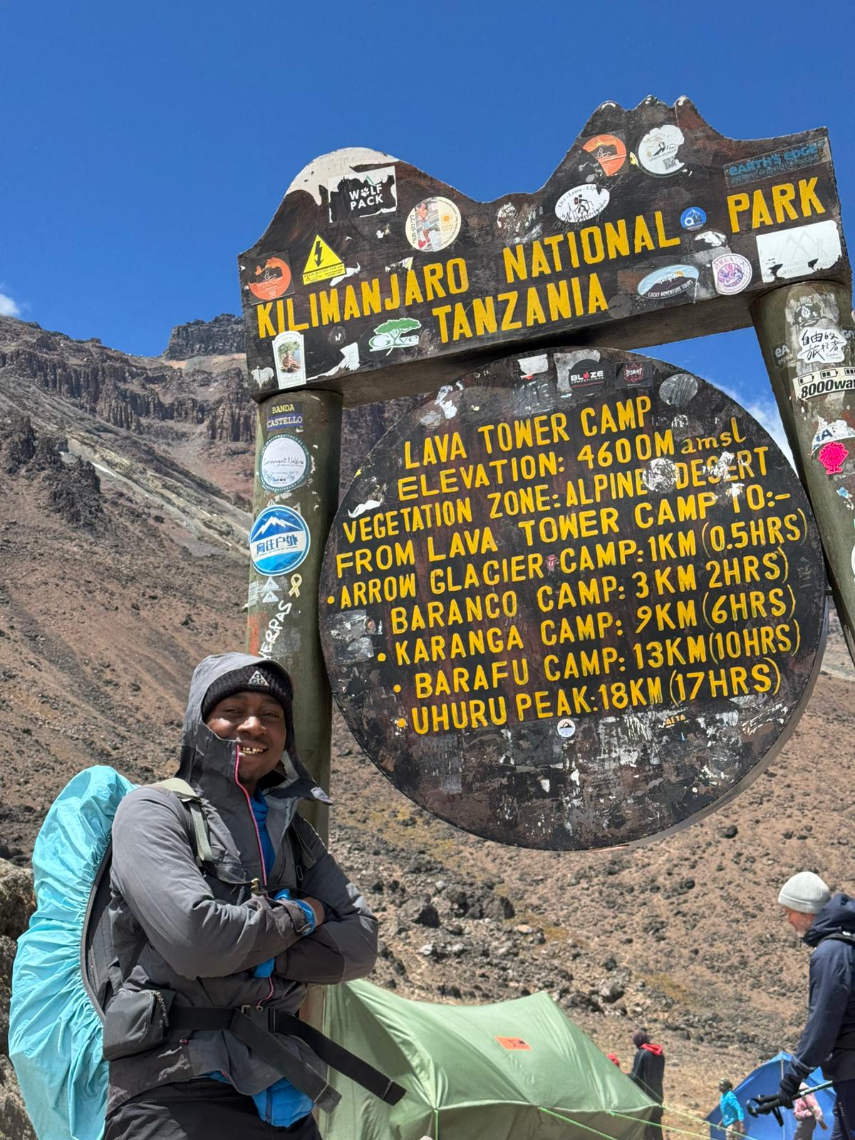 A climber standing beside a wooden sign in a rocky landscape