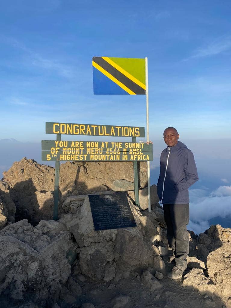 A mountain guide holding a Tanzanian flag beside a summit sign