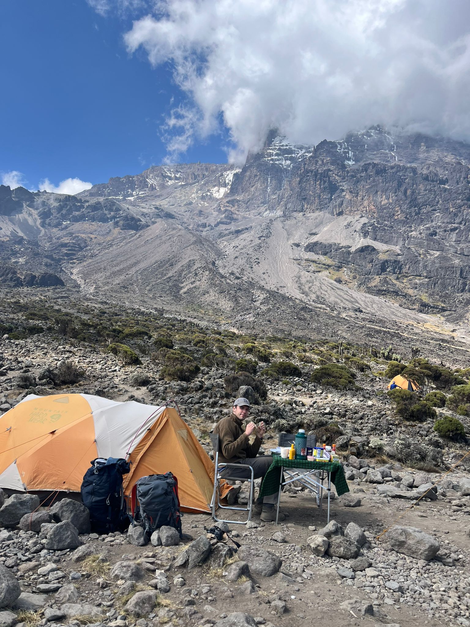 Orange tents and mountain crew below steep rocky slopes