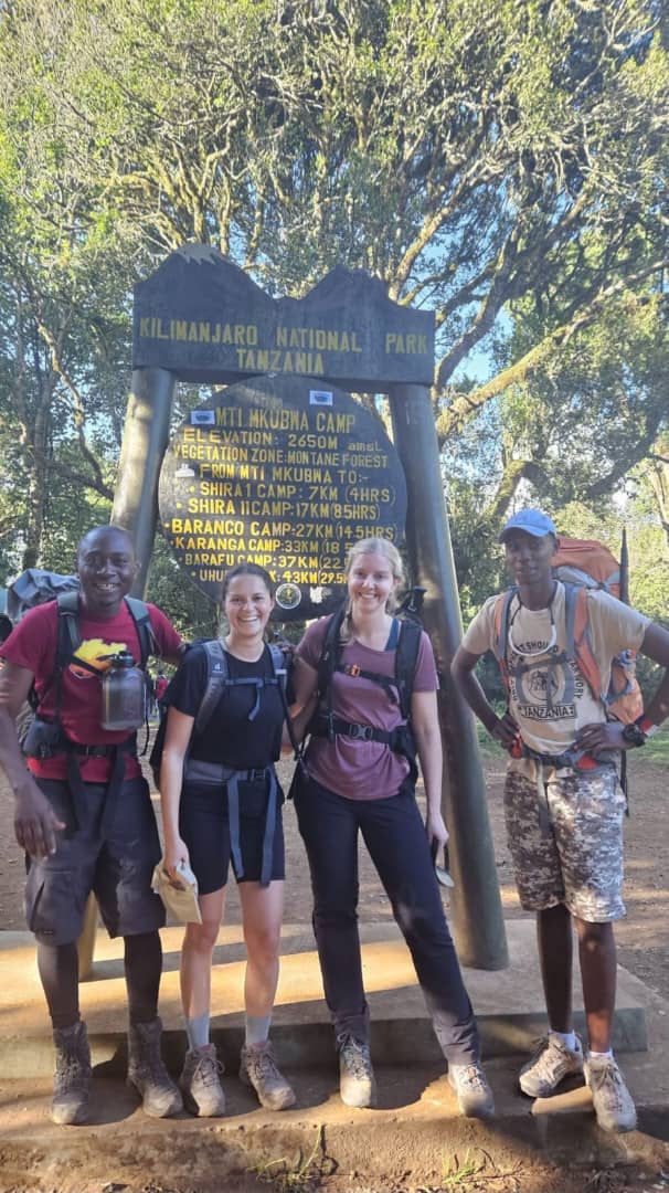 A group of hikers posing beside a large wooden sign among trees