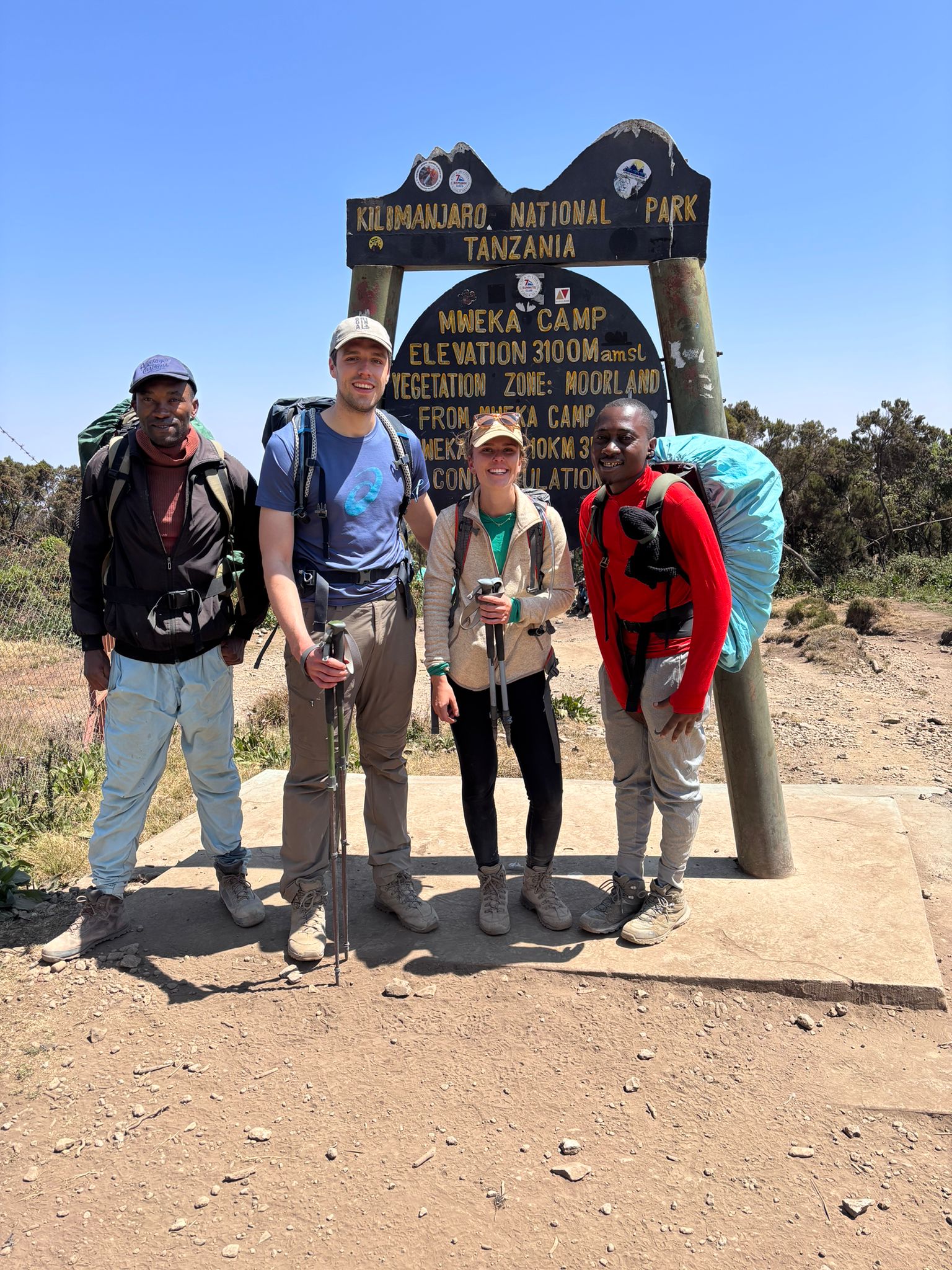 Four hikers standing together beside a large wooden trail sign
