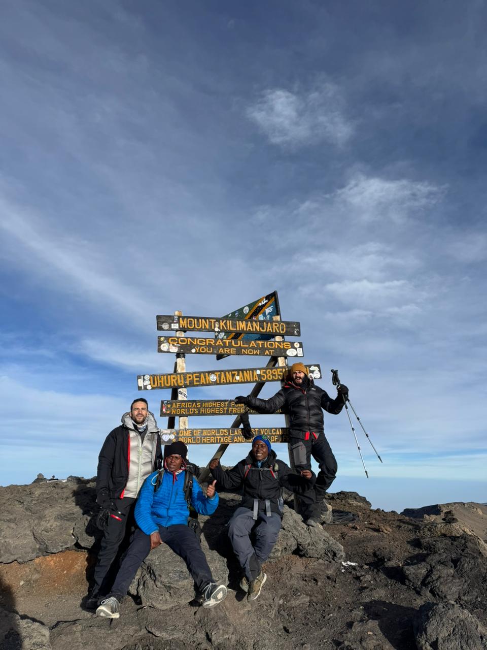 Climbers celebrating beside a cluster of wooden signs on rocky ground