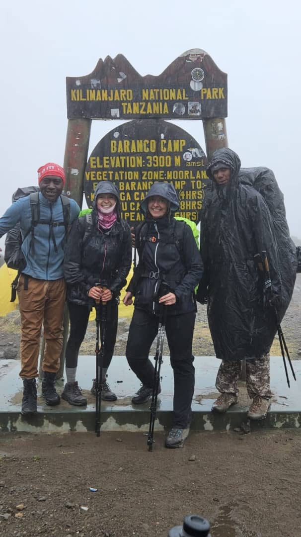 Four hikers in rain jackets standing beside a wet wooden sign