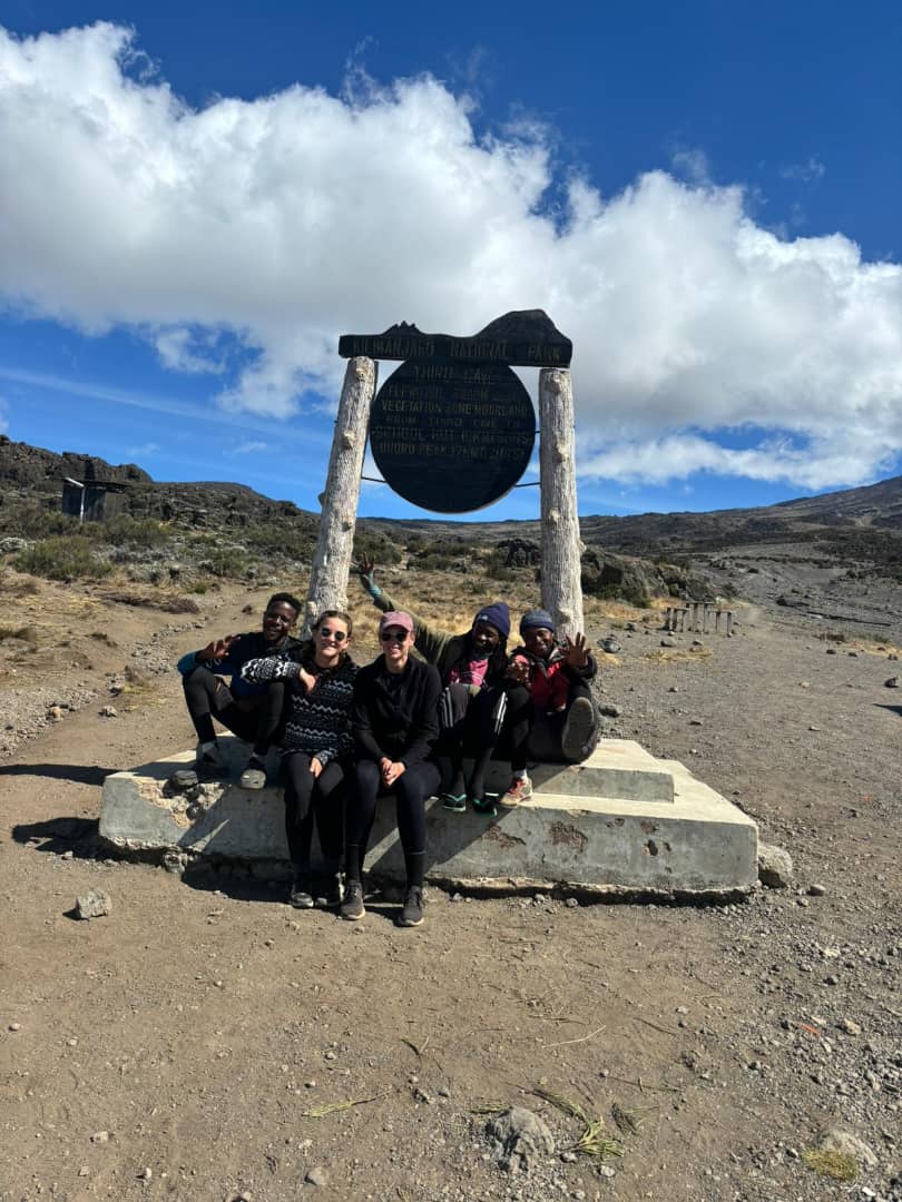 A group of friends sitting beneath a large metal mountain bell
