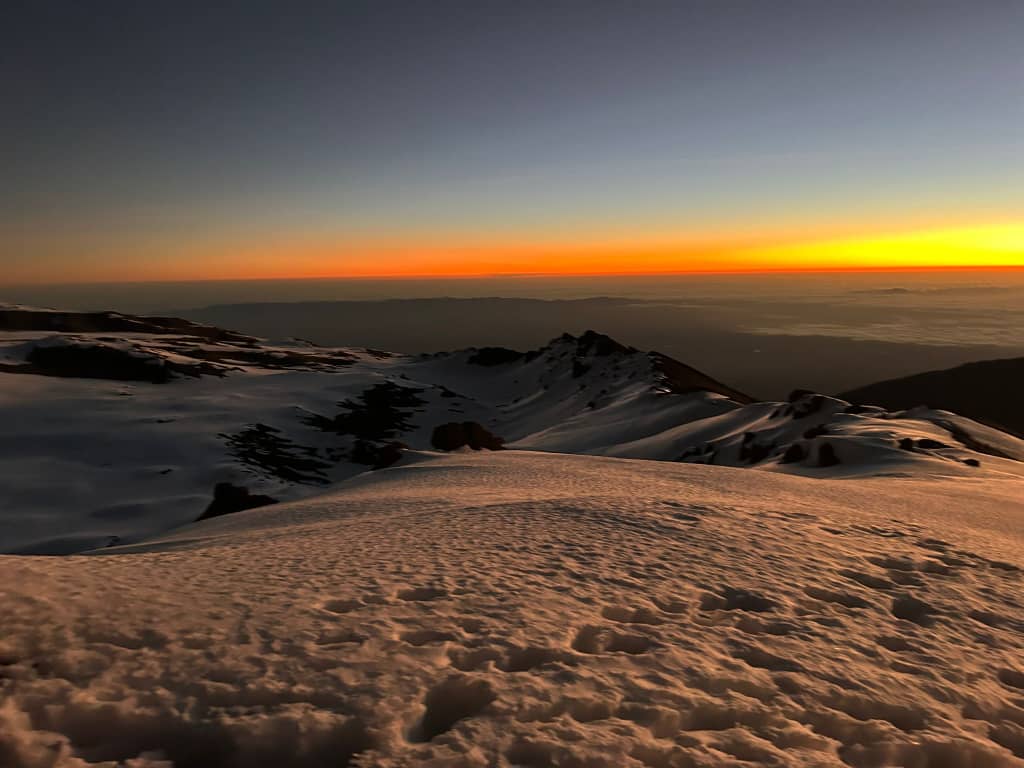 Orange sunrise light stretching across a wide snow-covered landscape