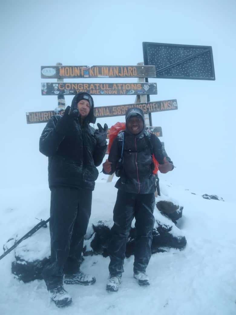 Two climbers standing beside a snow-covered wooden summit sign