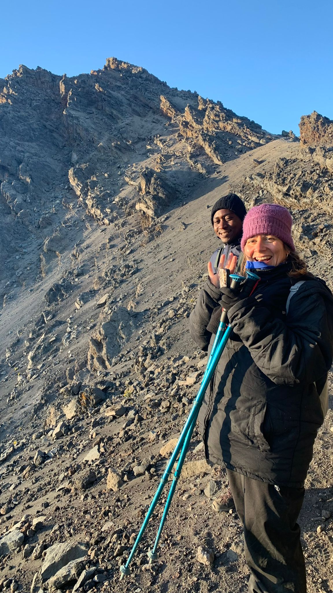Two climbers with trekking poles on a steep rocky mountain slope
