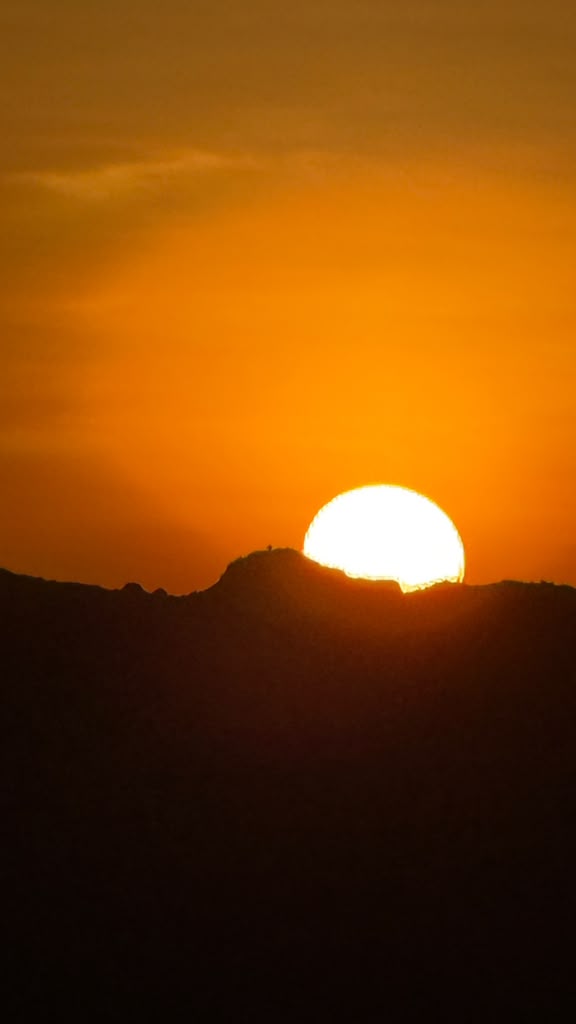 The sun appearing above a dark mountain ridge