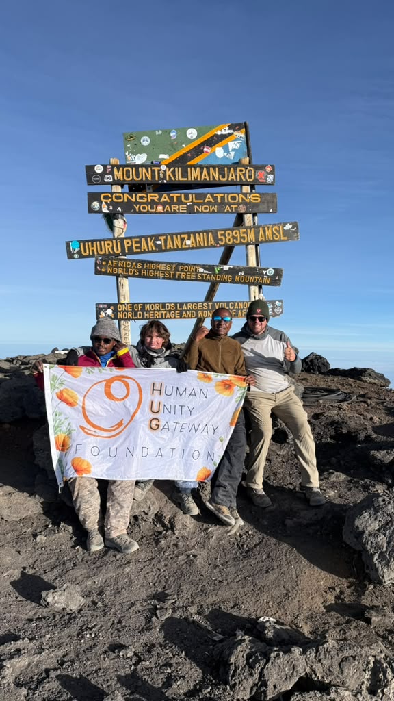 Climbers holding a banner beside a wooden summit sign