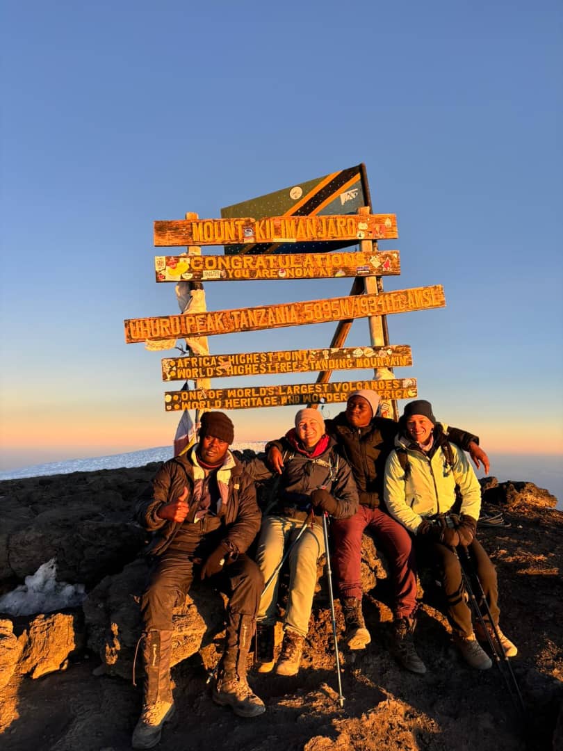 A group sitting together beside wooden summit signs in orange evening light